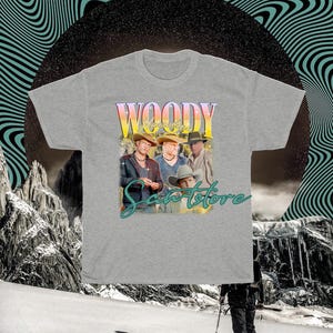 May include: A gray t-shirt with a graphic print of four men wearing cowboy hats. The text "Woody" and "Sante Store" are printed on the shirt.