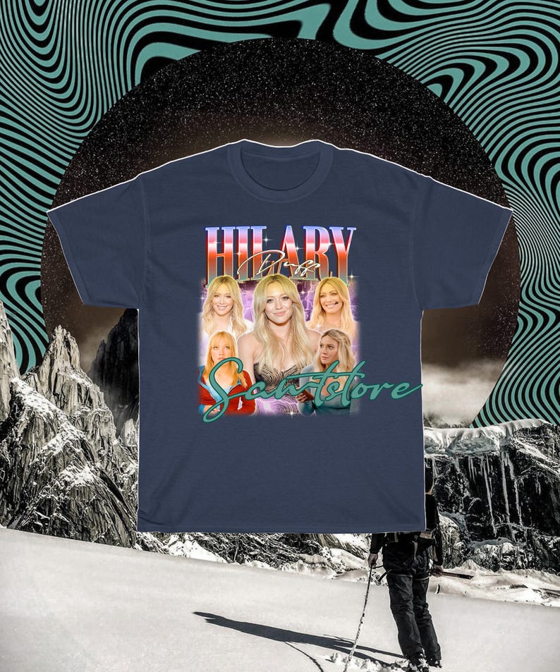 May include: Navy blue t-shirt with a retro design featuring the name "HILARY DUFF". The shirt includes multiple images of Hilary Duff and the text "Scents Store".