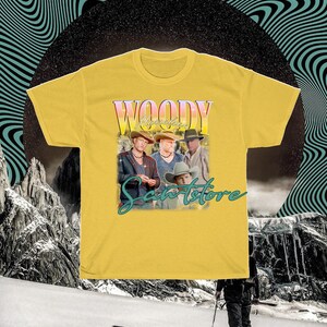 May include: Yellow t-shirt with a vintage-style graphic of four men wearing cowboy hats and the text "Woody Apparel &  Santorstore".