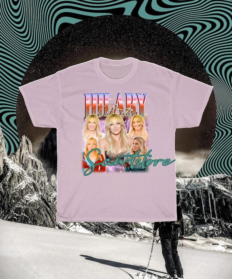 May include: A lilac t-shirt with a graphic of a woman, the name "HILARY" above her, and the text "Sweetstore" below. The graphic includes multiple images of the woman. The background has a black circle and a teal wavy design.