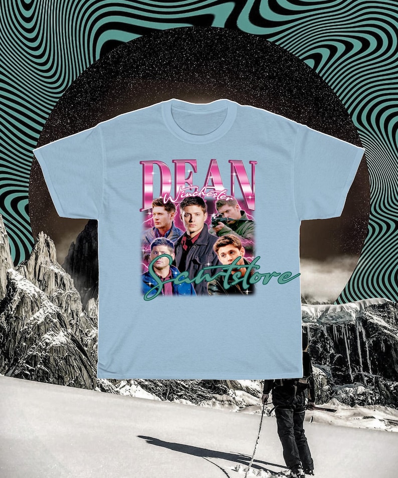 May include: Light blue t-shirt with a graphic print of Dean Winchester from the TV show Supernatural. The graphic features Dean and other characters from the show, with the text "Dean Winchester" and "Samstore" in a retro font.