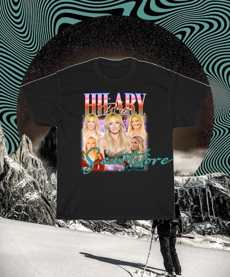 May include: Black t-shirt with a retro design. The design features the text "HILARY Duff" in a stylized font, along with multiple images of a blonde woman. The word "Scantstore" is written below in a script font.
