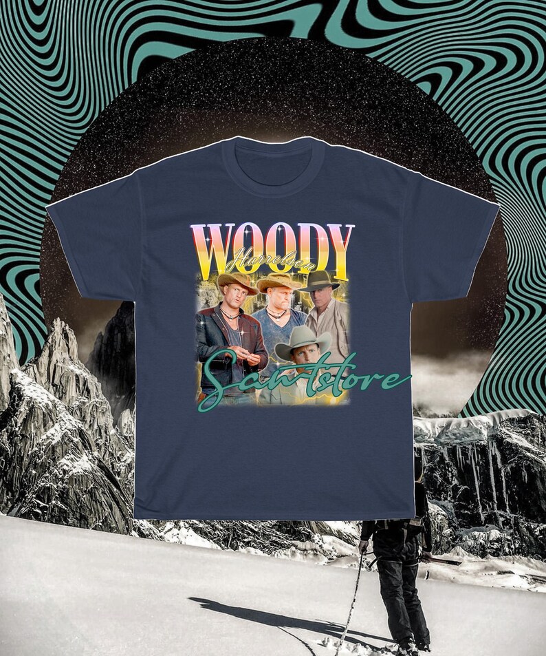 May include: A navy blue t-shirt with a vintage-style graphic of a band called "Woody & The Saints" with the text "Woody & The Saints" in a yellow and orange gradient. The band members are wearing cowboy hats and are standing in front of a sunset background.