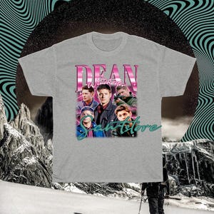 May include: A gray t-shirt with a graphic print of Dean Winchester from the TV show Supernatural. The graphic features Dean and other characters from the show, with the text "Dean Winchester" and "SaveStore" in pink and teal.