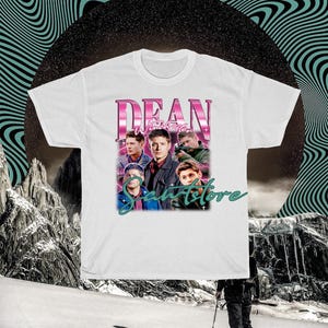 May include: White t-shirt with a pink graphic print of the characters from the TV show "Supernatural". The graphic features the text "Dean Winchester" and a group of men in a band.