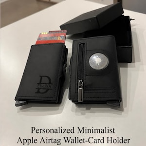 May include: Two black card holder wallets with a matte finish. One wallet features the engraved letter D with the name EVANSH below it. The other wallet includes a circular cutout for an Apple AirTag and a small vertical zippered pocket with a silver pull.