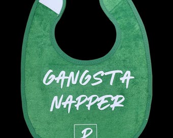 May include: Green baby bib with white trim and the words "GANSTA NAPPER" in white script. The bib has a white patch at the neck and a small logo at the bottom that says "PAIGE MARIE".