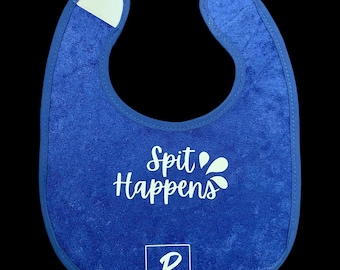 May include: A blue terry cloth baby bib with white text that reads "Spit Happens" and two white droplet graphics. The bib has a white patch at the neck and a "P" logo with the name "Paige Marie" below.