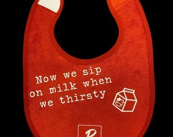 May include: Red baby bib with white text that reads "Now we sip on milk when we thirsty." A white graphic of a milk carton with a cow is on the right. The brand logo "P" is at the bottom.
