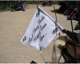 May include: A white flag with black script that reads "And They Rode Happily Ever After..." is attached to a motorcycle. The flag has decorative heart designs. A fluffy white tail is attached to the motorcycle.