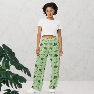Könnte beinhalten: Hellgrüne Palazzo-Hose mit einem sich wiederholenden Muster einer Zeichentrickfigur mit Hut. Die Hose wird mit einem weißen Crop-Top und weißen Turnschuhen kombiniert. Die Hose ist aus einem weichen, fließenden Stoff gefertigt.