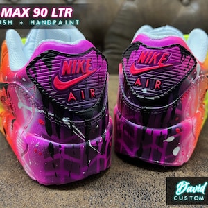 May include: Custom painted Nike Air Max 90 LTR sneakers with a vibrant rainbow gradient and black splatters. The back of the shoe features a black Nike swoosh with a pink outline and the text "NIKE AIR" in black.