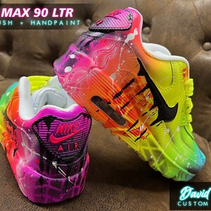 May include: A pair of custom-painted Air Max 90 LTR sneakers with a vibrant rainbow and neon color scheme. The shoes feature a black Nike swoosh and black accents. The shoes are painted with a splatter effect and have a drip effect on the back.