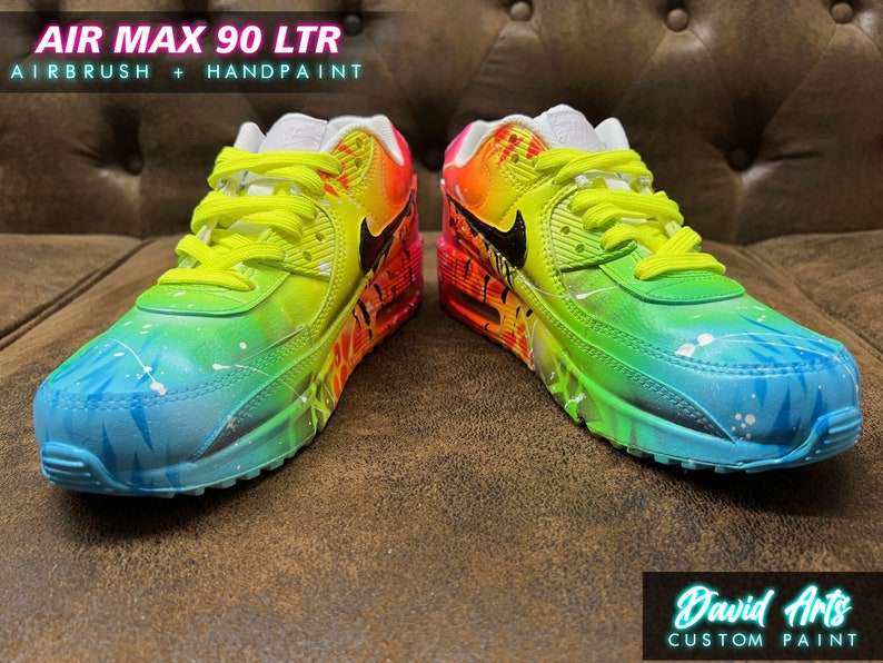 May include: Custom painted Air Max 90 LTR sneakers with a rainbow gradient design. The shoes feature a blue, green, yellow, orange, and pink color scheme with white accents. The Nike swoosh logo is black. The text "AIR MAX 90 LTR" and "AIRBRUSH + HANDPAINT" is visible on the image.
