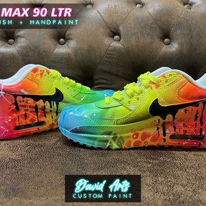 May include: Custom painted Air Max 90 LTR sneakers with a rainbow gradient and black drip paint. The shoes feature a white base with a black swoosh logo and are labeled "AIR MAX 90 LTR AIRBRUSH + HANDPAINT".