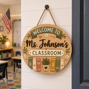 May include: A round wooden classroom sign with the text "WELCOME TO Ms. Johnson's CLASSROOM" in black and white. The sign has a rope hanger and features decorative elements like books, flowers, and a potted plant.