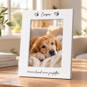 May include: A white rectangular picture frame featuring the name Cooper flanked by two heart-shaped paw prints at the top and the text Forever loved, never forgotten at the bottom. The frame displays a photograph of a golden dog resting on a blanket.