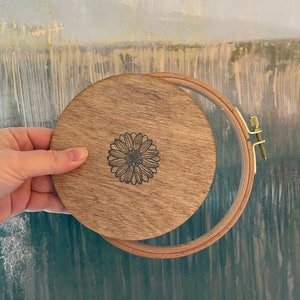 May include: A wooden embroidery hoop with a natural wood finish. The hoop has a floral design engraved on the front.