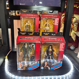May include: Four DC Comics Multiverse action figures in their original packaging. Two figures are Wonder Woman, and the other two are Steve Trevor and a male figure. The boxes are red and black with the DC Comics Multiverse logo.