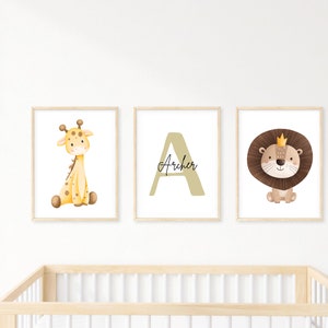 May include: Three framed nursery art prints. One shows a giraffe, another a letter "A" with the name "Archer", and the third a lion wearing a crown. The prints have light wood frames and are on a white wall.
