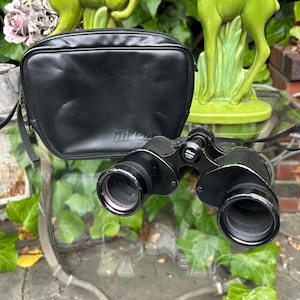 May include: Black binoculars with a black leather case. The binoculars have the word "Nikon" printed on the case and the words "Nikon 8x25" printed on the binoculars.