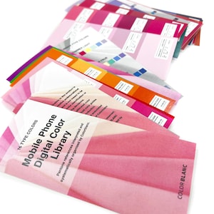 May include: A collection of color swatches fanned out, displaying a range of pink and magenta hues. The text "Mobile Phone Digital Color Library" is visible on the front swatch. Other swatches show color gradients and text labels, with a white background.