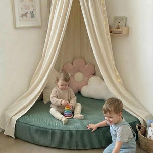May include: A children's play area with a teal corduroy mat and a draped canopy. Two children play with a wooden toy train and a stacking toy. The scene includes decorative pillows and framed artwork. The mat is approximately 150 cm in diameter.