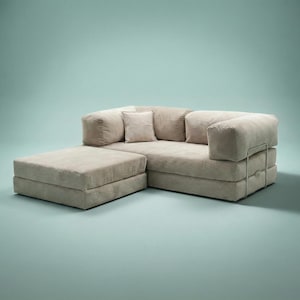 May include: A beige sectional sofa with an attached ottoman. The sofa has a low profile with square cushions and a metal armrest. The ottoman is rectangular and matches the sofa's color and fabric. The background is a solid light teal.