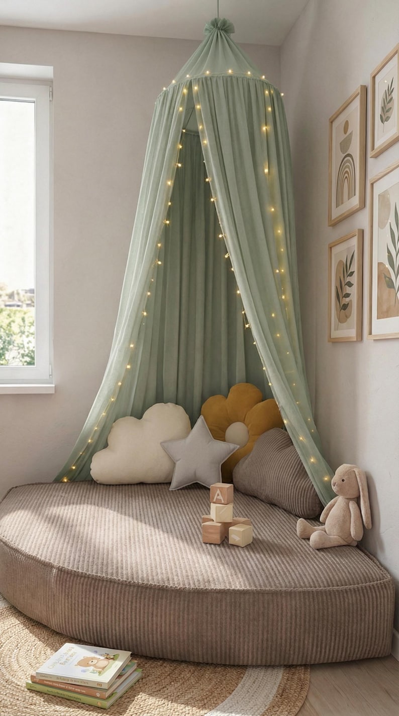 May include: A child's reading corner featuring a sage green canopy with fairy lights. It has cloud, star, and flower-shaped cushions, wooden blocks, and a stuffed rabbit. The bed is a round, corduroy-covered cushion.