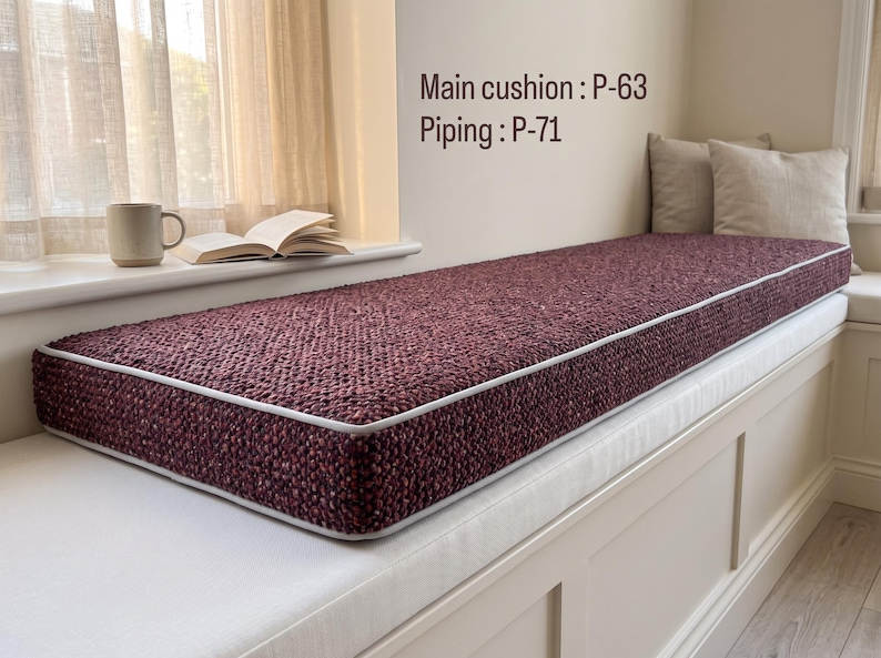 Pode incluir: Uma almofada retangular para banco de janela com tecido texturizado em bord&ocirc; escuro e debrum claro. O texto na parede diz Main cushion : P-63 e Piping : P-71. A almofada est&aacute; posicionada sobre um banco embutido de cor branca.