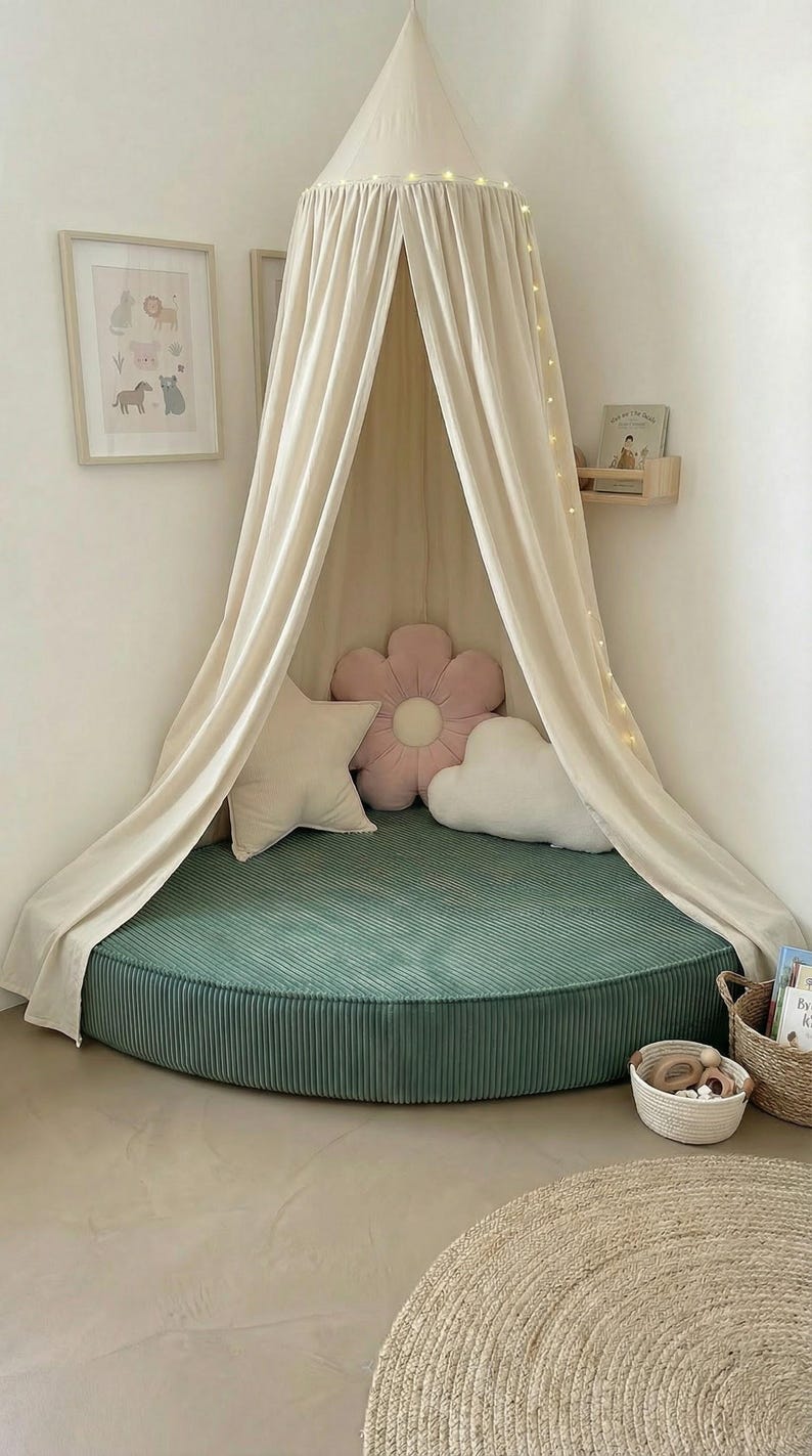 May include: A children's reading corner featuring a green corduroy floor cushion, a cream canopy, and decorative pillows shaped like a star, flower, and cloud. A framed animal print and fairy lights create a cosy space.