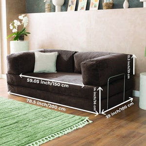 May include: A brown corduroy sofa with dimensions of 78.5 inches (200 cm) long, 59.05 inches (150 cm) wide, and 15.3 inches (39 cm) high. It features a light-colored square pillow and a metal armrest. A green rug is in front of the sofa.