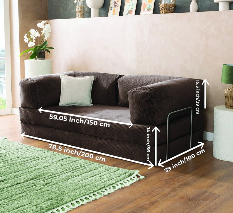 May include: A brown corduroy sofa with dimensions of 78.5 inches (200 cm) long, 59.05 inches (150 cm) wide, and 15.3 inches (39 cm) high. It features a light-colored square pillow and a metal armrest. A green rug is in front of the sofa.
