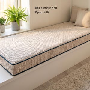 Pode incluir: Uma almofada retangular bege texturizada para banco de janela com debrum azul escuro. O texto na parede diz Main cushion : P-50 e Piping : P-67. Duas almofadas quadradas bege a condizer est&atilde;o colocadas na extremidade da almofada.