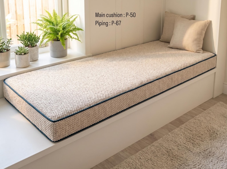 Pode incluir: Uma almofada retangular bege texturizada para banco de janela com debrum azul escuro. O texto na parede diz Main cushion : P-50 e Piping : P-67. Duas almofadas quadradas bege a condizer est&atilde;o colocadas na extremidade da almofada.