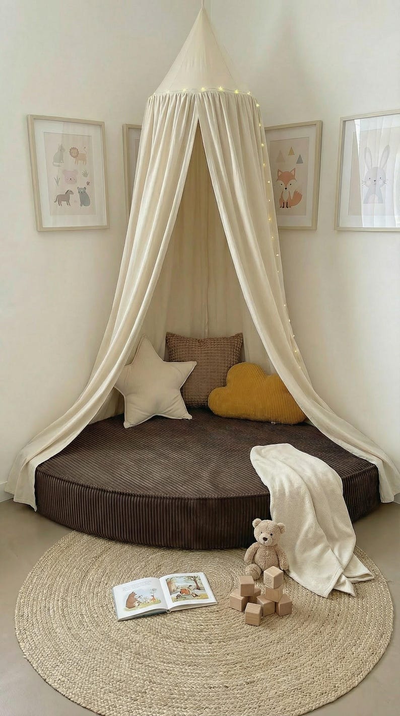 May include: A children's reading nook featuring a brown corduroy bed, cream canopy, and decorative pillows. A jute rug, teddy bear, and framed animal art complete the space. Fairy lights provide a soft glow.