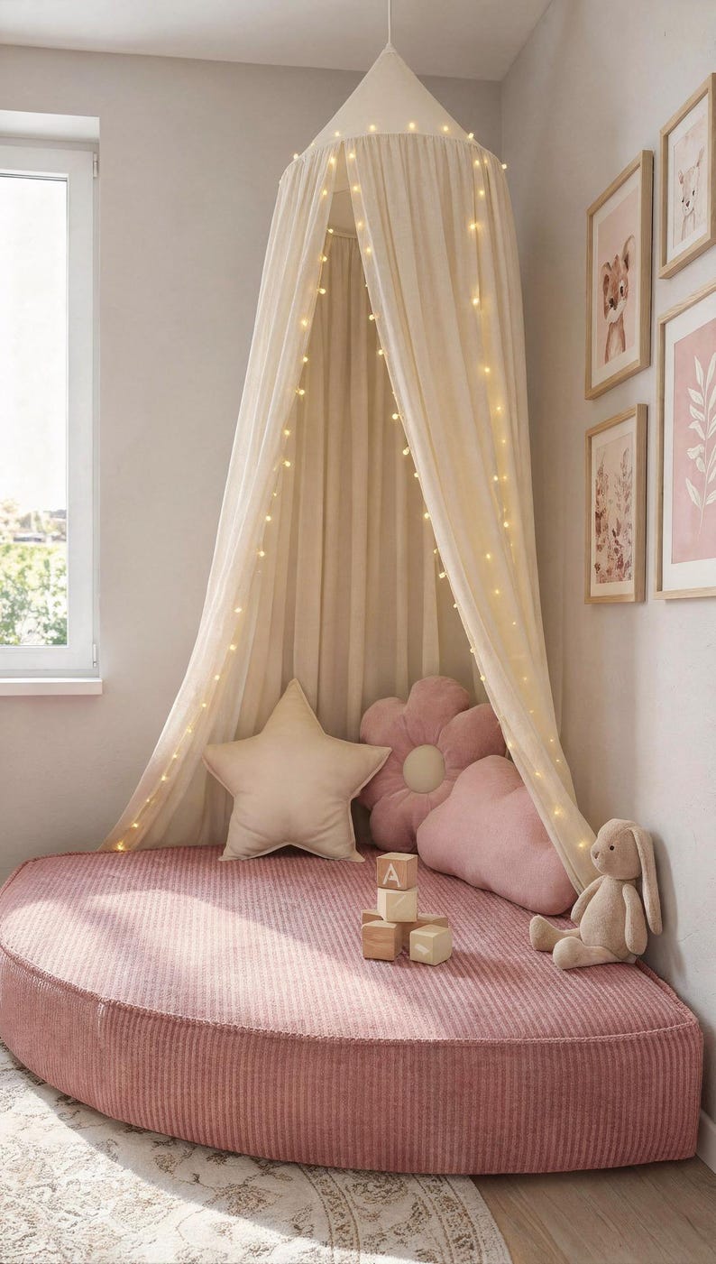 May include: A child's reading nook featuring a pink corduroy bed, star and flower-shaped cushions, and a cream canopy with fairy lights. Framed artwork and a stuffed bunny create a welcoming atmosphere. The bed is approximately 150 cm in diameter.