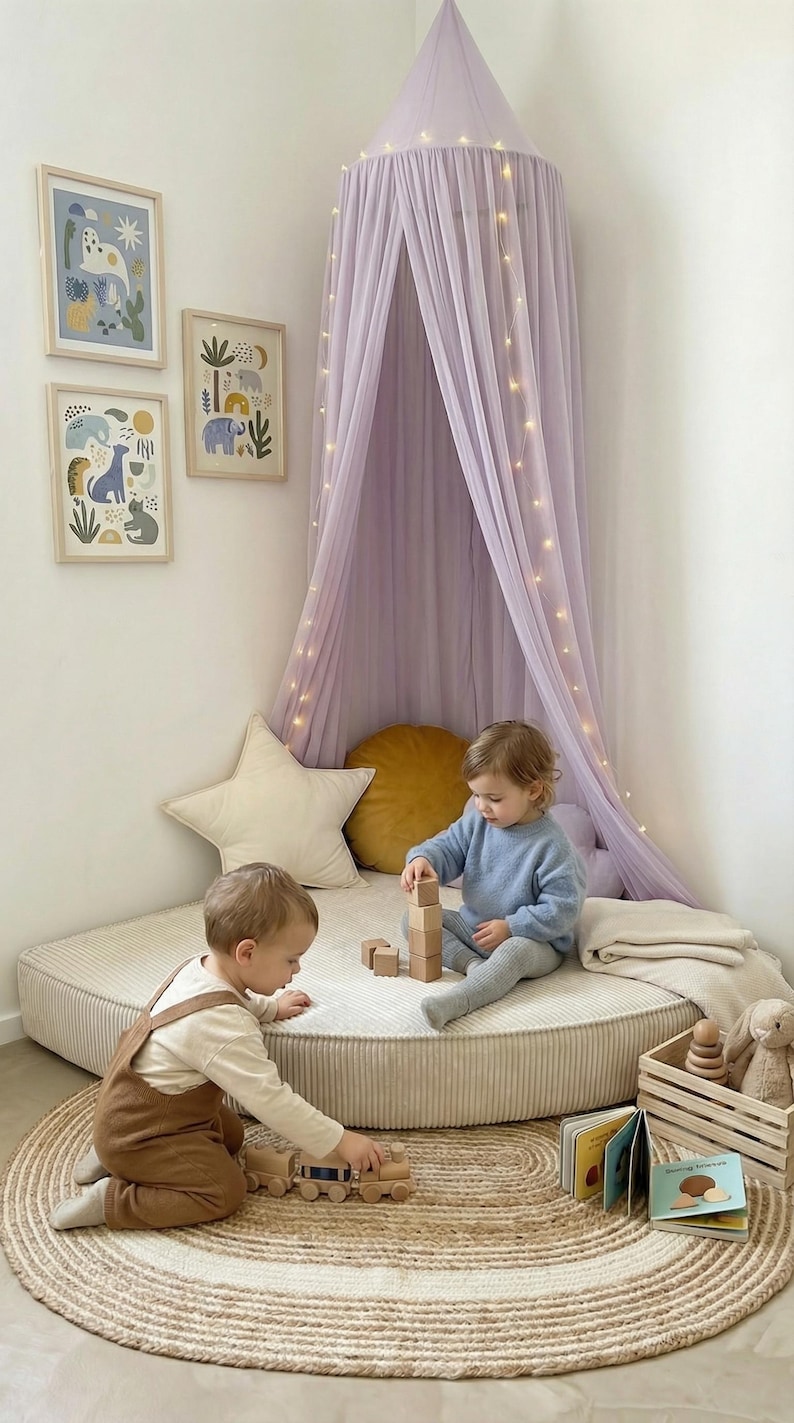 May include: A nursery scene with two children playing. A lilac canopy with fairy lights is suspended above a circular play mat. The room includes framed animal prints, a star cushion, and a wooden toy train.