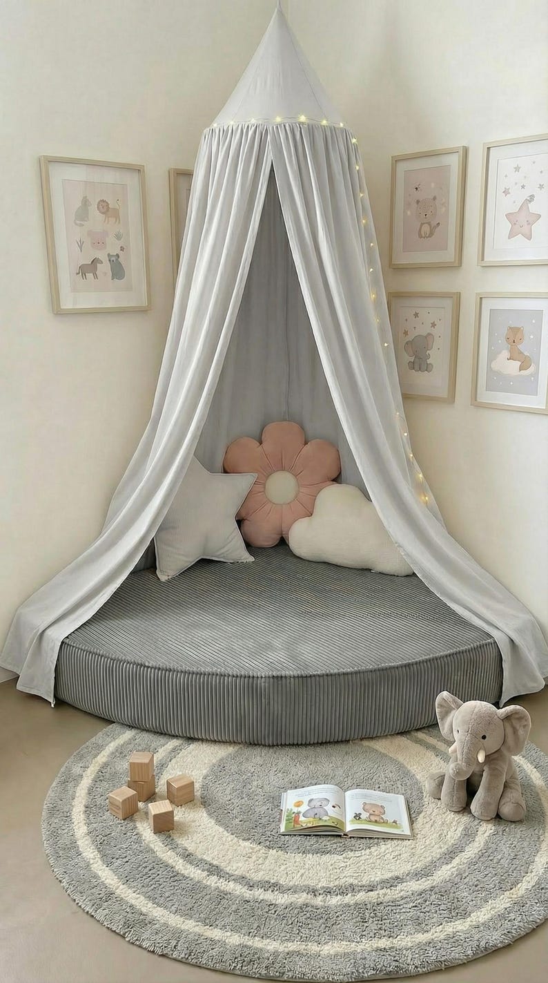 May include: A grey, circular children's play area with a canopy, pillows, and a rug. The canopy drapes over a circular bed. Framed animal prints decorate the wall. A plush elephant toy and wooden blocks are on the rug.
