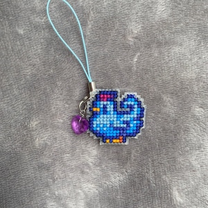 Peut inclure: Un charme en forme de poulet brod&eacute; en bleu et violet avec un charme en forme de c&oelig;ur violet attach&eacute; &agrave; une ficelle bleu clair.