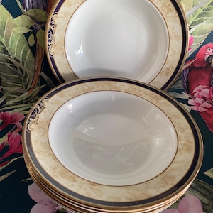 Puede incluir: Un conjunto de seis tazones de sopa blancos con un borde dorado y azul. Los tazones tienen un patrón decorativo en el borde.