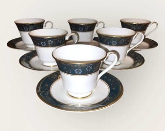 May include: A six-piece tea set with white cups and saucers. Each piece has a dark teal band with a floral design and gold edging. The cups have a traditional handle shape.