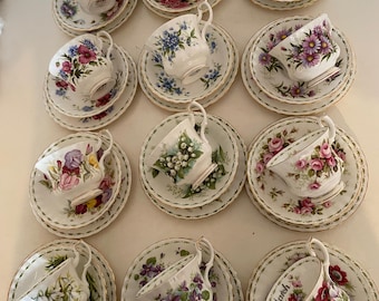 Puede incluir: Una colección de tazas y platillos vintage, cada uno con un diseño floral único. Las tazas presentan diversas flores como rosas y violetas, con adornos dorados. Los platillos complementan las tazas. La palabra "March" es visible en una taza.