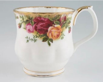 May include: A white teacup with a gold rim and floral design featuring red, pink, and yellow roses. The cup has a fluted design and a handle.
