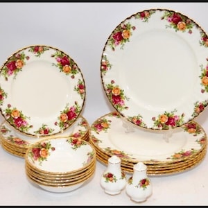 Pode incluir: Um conjunto de louça de porcelana branca com um padrão floral de rosas em tons de vermelho, laranja e rosa. Os pratos e as tigelas têm bordas douradas. Inclui pratos, tigelas e saleiros e pimenteiros.