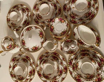 Puede incluir: Un juego de porcelana vintage con un diseño floral de rosas rojas, rosas y amarillas sobre fondo blanco. El conjunto incluye tazas, platillos, platos, una tetera, una fuente para servir y saleros y pimenteros, todos con ribetes dorados.