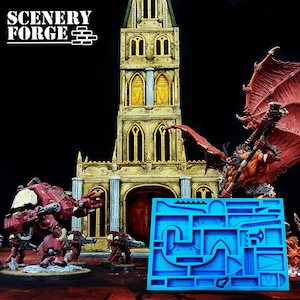 Op de afbeelding: Een blauwe siliconen mal met diverse vormen en een gedetailleerd miniatuurkasteel met figuren. De afbeelding toont ook een rood-gouden demonenfiguur en een rode oorlogsmachine. Het Scenery Forge-logo staat linksboven.