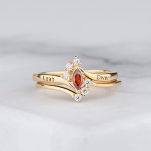 May include: A gold ring set with a red gemstone and small clear stones. The ring is engraved with the names "Leah" and "Owen".