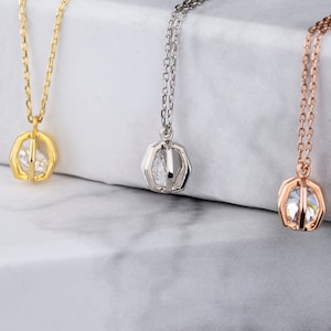 Puede incluir: Tres delicados collares con un pequeño colgante de piedra preciosa transparente en un marco hexagonal. Los collares se muestran sobre una superficie de mármol blanco. Los collares están disponibles en oro, plata y oro rosa.