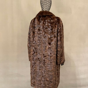 May include: A long brown fur coat with a collar. The coat is on a mannequin.